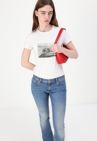 T-shirt blanc avec impression photo en noir et blanc, associé à un jean bleu et un sac à épaule rouge. Texture lisse et coupe décontractée.