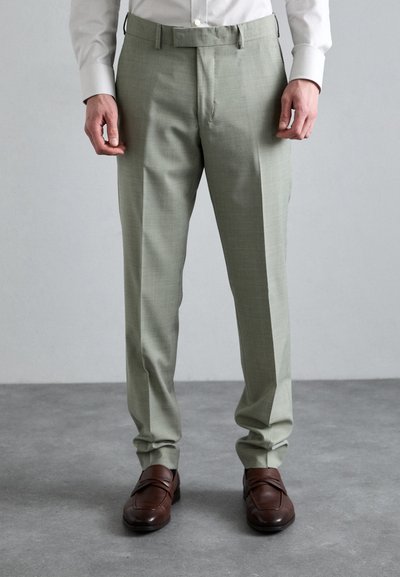 Hellgrüne maßgeschneiderte Hose mit subtiler Textur, gerade geschnitten und mit Gürtelösen, kombiniert mit dunkelbraunen Schuhen.
