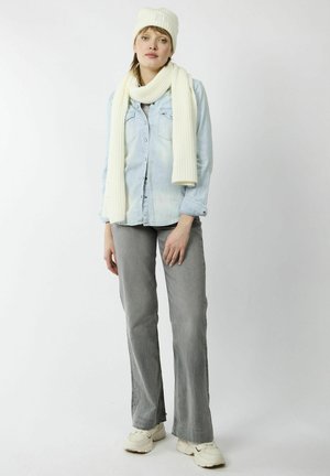 Helle blaue Jeanshemd, cremfarbene Strickmütze und -schal, graue weit geschnittene Hose und hellfarbene Sneakers. Einfaches Design, keine sichtbaren Muster.