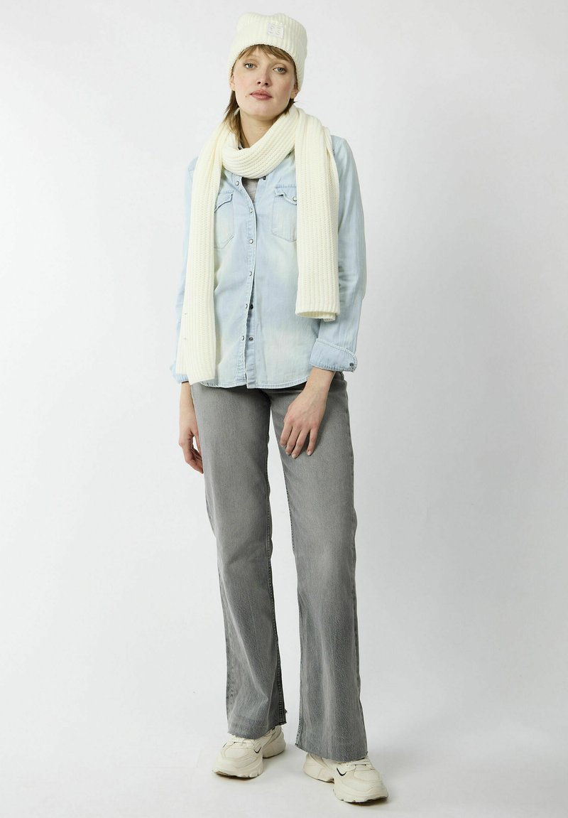 Chemise en denim bleu clair, bonnet et écharpe en tricot crème, pantalons gris à jambes larges et baskets de couleur claire. Design simple, aucun motif visible.