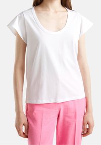 White short-sleeve t-shirt with a wide scoop neckline, made of soft cotton fabric. Worn with light pink, loose-fitting pants.