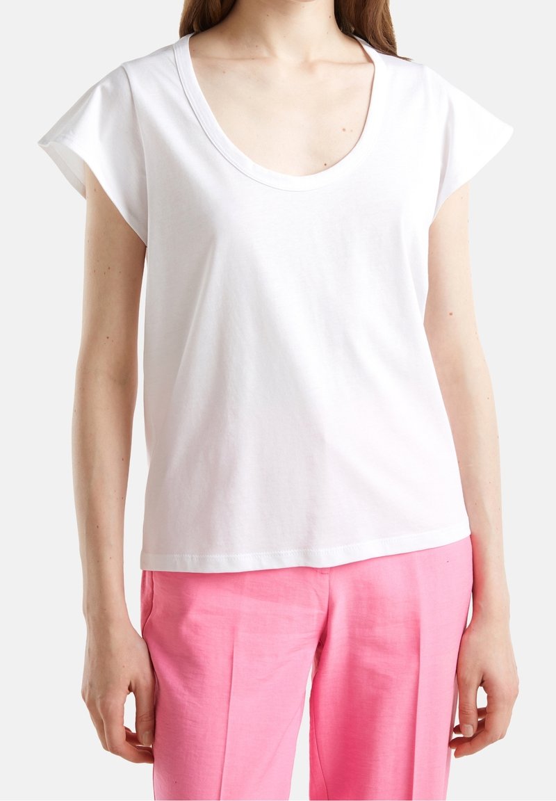 White short-sleeve t-shirt with a wide scoop neckline, made of soft cotton fabric. Worn with light pink, loose-fitting pants.