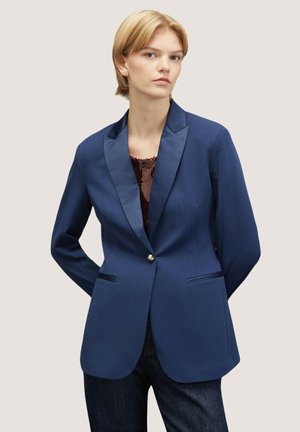 Blazer sartorial di colore blu navy con revers in satin, chiusura con bottoni frontali e due tasche anteriori. Texture liscia, forma strutturata e design elegante.
