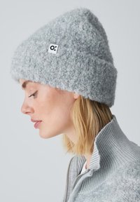 Gray knitted beanie with a textured, fluffy surface, featuring a small, square logo. The design is fitted and slightly slouchy at the top.