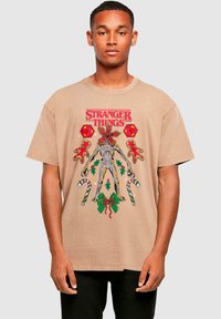 Béžové bavlněné tričko s pestrou grafikou tvora, cukrovinek a vánočních prvků, s textem "Stranger Things".