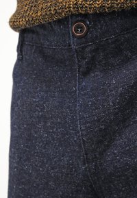 Dark blue textured trousers with a visible button at the waist, featuring a subtle pattern and a soft, woven fabric appearance.
