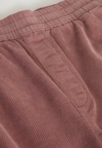 Primer plano de pantalones de pana rosa polvo con cinturilla elástica y detalles visibles de costuras frontales.