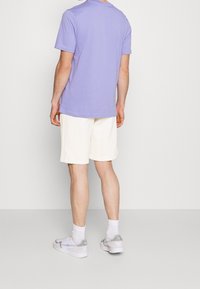 Lila bomullströja, krämfärgade shorts, grå sneakers och vita strumpor. Enkelt mönster med rund halsringning och avslappnad passform.