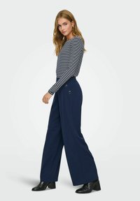 Navy wide-leg pants with button accents at the waist, paired with a navy and white striped long-sleeve shirt. Solid dark color and relaxed fit.