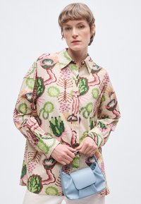 Buntes Hemd mit Blumen- und Pflanzenmustern; Knopfleiste; lange Ärmel; kombiniert mit einer kleinen blauen Lederhandtasche.