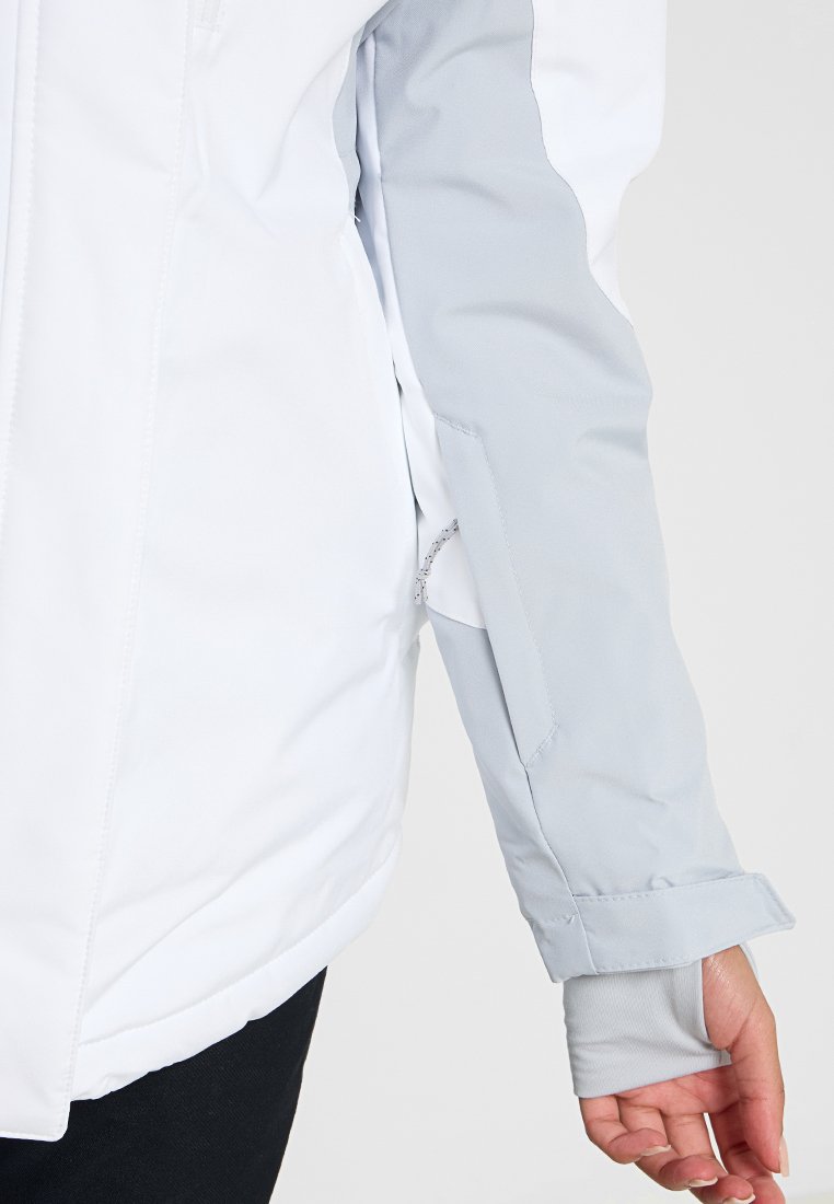 Weißer Blazer mit hellgrauem Ärmelpanel und verstellbarem Bündchen, getragen von einer Person mit sichtbarem Hand an der Seitennaht.