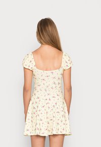 Květinové šaty v jemně žluté barvě s krátkými nabíranými rukávy, čtvercovým výstřihem a rozšířenou sukní. Obsahuje malé růžové a zelené květinové vzory.