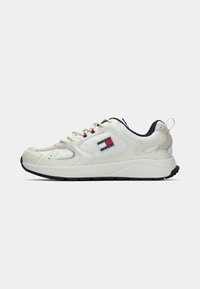 Bijela tenisica s crnim potplatom, kremastim vezicama, crvenim otvorima i Tommy Jeans logom na strani.