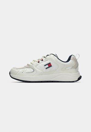 Bijela tenisica s crnim potplatom, kremastim vezicama, crvenim otvorima i Tommy Jeans logom na strani.
