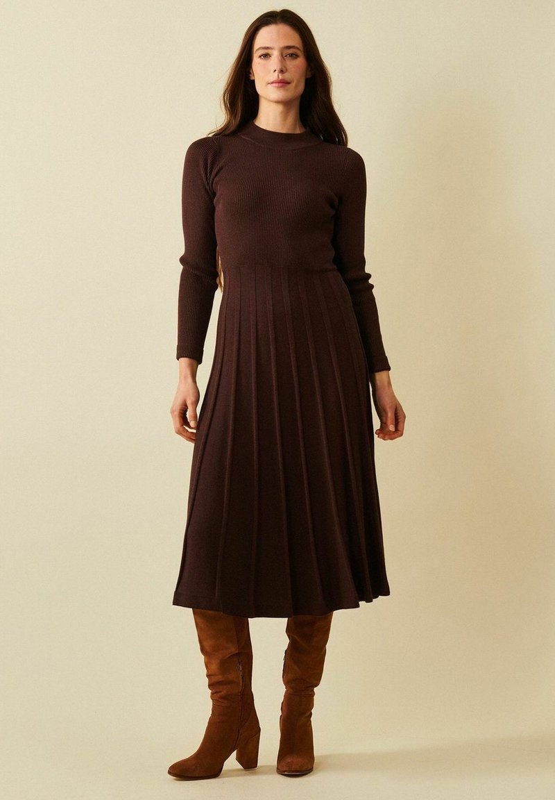 Ruske ribbede strikkekjole med lange ermer, tettsittende overdel og utsvingt plisséskjørt. Båret med brune semskede støvler opp til knærne.