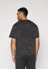T-shirt en coton noir style usé avec des manches courtes, col rond et un aspect délavé. Il présente une coupe décontractée et des coutures visibles.