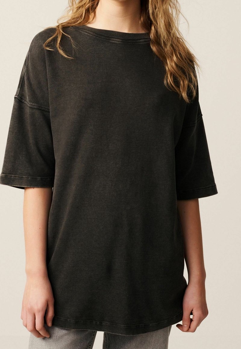 Oversized black cotton t-shirt with a scoop neckline and short sleeves, featuring a faded texture and visible stitching on the seams.