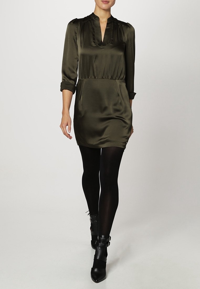 Abito in satin verde oliva con scollatura a V, vita arricciata e maniche lunghe. Indossato con collant neri e stivaletti alla caviglia con accenti di fibbia.