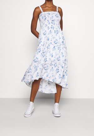 Robe fleurie blanche avec motifs bleus, design à volants et bretelles réglables, associée à des baskets montantes blanches. Tissu texturé.