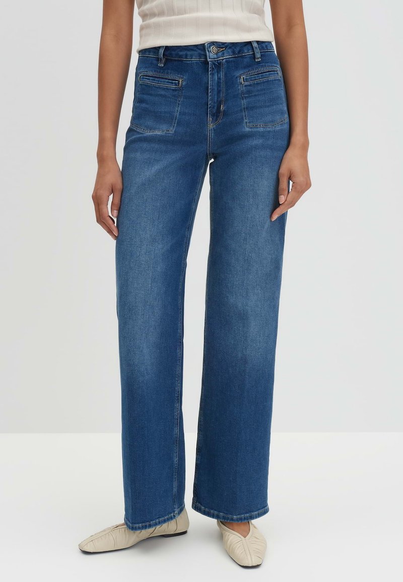 Wijd-uitlopende blauwe denim jeans met een hoge taille, voorzien van voor- en achterzakken, strakke lijnen en contraststiksels. De textuur is stevig en glad.