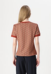 Krátký rukáv, upnutý top v rezavé barvě s geometrickým vzorem. Má kulatý výstřih a kontrastní lemování na ramenou. Hladká textura.