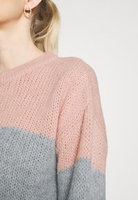 Maglione lavorato a maglia con strisce rosa e grigie, scollo rotondo e tessuto testurizzato. Orecchini circolari dorati completano il look.