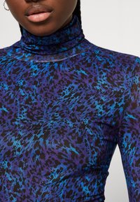 Pitkät hihat, korkea kaula-aukko, tekstiilipinta, jossa on violetti ja sininen eläinkuoski mustalla taustalla.