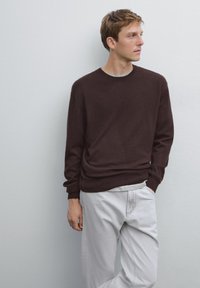 Maglione lavorato a maglia marrone con collo rotondo, abbinato a jeans grigi chiari. Il maglione ha una vestibilità comoda e una texture morbida. Design semplice, senza fantasie.