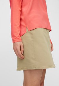 Korálový top s dlouhým rukávem doplněný béžovou sukní. Top má zaoblený lem a boční rozparky, zatímco sukně má hladkou texturu a rovný střih.