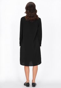 Fekete, hosszú ujjú ruha laza szabással és inggallérral; sima textúrával és egyenes hemline-nel, lapos fekete cipővel párosítva.