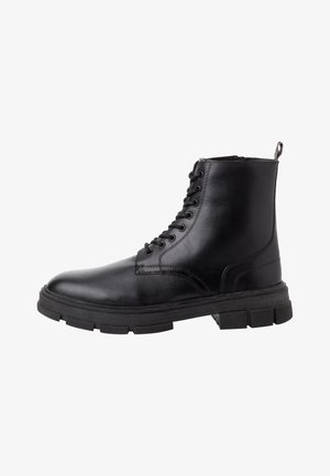 Bottine noire en cuir avec un bout rond, un laçage à l'avant et une semelle en caoutchouc épaisse. Présente des détails de couture et une languette à l'arrière.