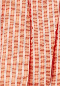 Tissu de couleur pêche avec un motif texturé, présentant des rayures verticales blanches, créant un effet froissé.