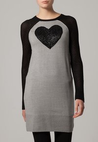 Robe tricotée grise avec un design de cœur en sequins noirs, présentant des manches en tulle noir et un ourlet côtelé. Texture lisse avec des éléments contrastés.