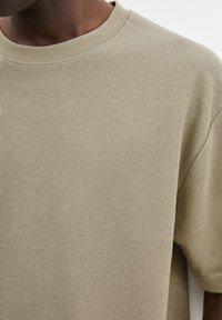 Beige ribbet t-shirt med korte ærmer og rund hals, med tekstureret stof og synlige sømdetaljer.