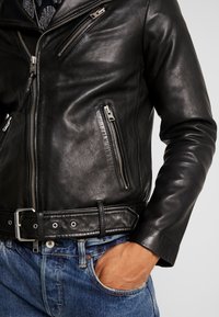 Svart läderbikerjacka med en figursydd design, dragkedjefickor och ett brett bälte. Slät textur med silverdetaljer.