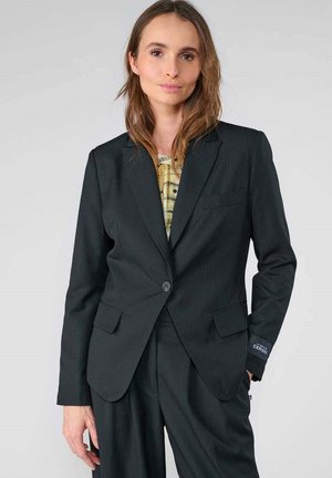 Schwarzer Blazer mit Nadelstreifen, einem Knopf, zwei vorderen Taschen und tailliertem Schnitt. Getragen über einem gemusterten Oberteil, glatte Stoffoberfläche.