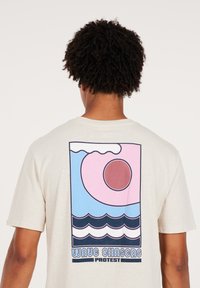 Cream-colored t-shirt featuring a graphic design with pink and blue waves, a circular sun, and the text "WAVE CHASERS PROTEST" at the bottom.