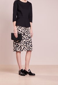 Schwarzes Peplum-Oberteil, Bleistiftrock mit Leopardenmuster, schwarze Clutch und glänzende schwarze Slipper. Glattes Material und strukturierter Schnitt.