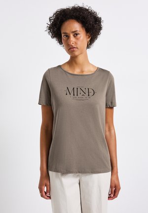 Camiseta de algodón verde oliva con cuello redondo y mangas cortas. Presenta un texto impreso en negro que dice "HAZ DE TU MENTE UN LUGAR AGRADABLE PARA ESTAR."