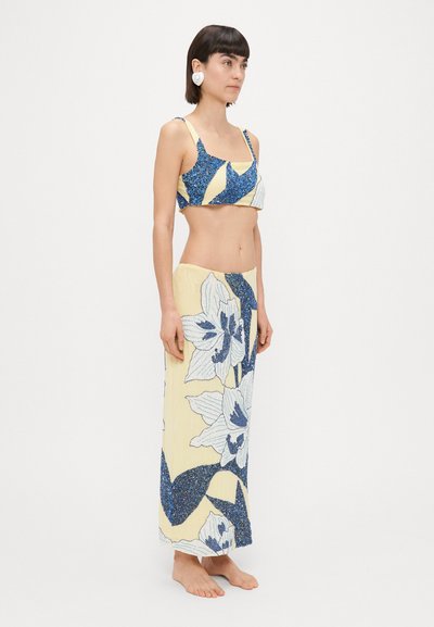 Conjunto de dos piezas que incluye un crop top brillante en azul y amarillo con un diseño floral y una falda larga a juego con patrones de flores en azul y blanco.