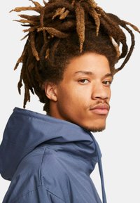 Chaqueta con capucha de tejido azul oscuro con un acabado texturizado. Presenta una capucha ajustable con cordón y un corte relajado.