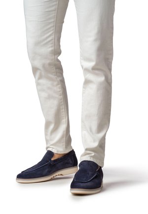 Granatowe mokasyny z zamszu z białą gumową podeszwą, charakteryzujące się wsuwanym fasonem i delikatnymi teksturowanymi akcentami. Noszone z dopasowanymi białymi spodniami.