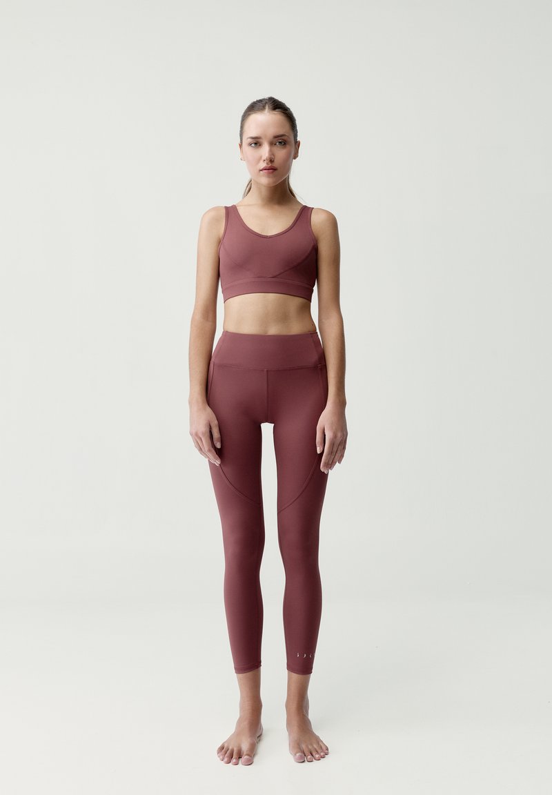 Bordový set športového oblečenia obsahujúci priliehavú športovú podprsenku s okrúhlym výstrihom a legíny s vysokým pásom a zakrivenými švovými detailmi. Hladká textúra.