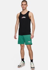 Top a maniche corte nera senza maniche con logo "FILA" bianco e rosso; pantaloni corti in rete verdi; sneakers bianche con dettagli verdi; design minimalista.