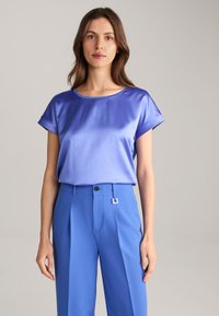 Satijnen top met korte mouwen in lichtblauw, gecombineerd met hoog- taille, gestructureerde blauwe broek met een rechthoekige gesp en plooien.