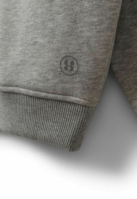 Tissu de sweat-shirt gris avec des poignets côtelés, présentant un logo noir circulaire sur la manche. Texture douce et design décontracté.