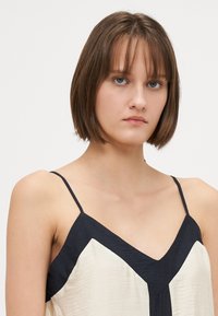 Camasă de satin cu un model în zigzag în negru și crem, cu bretele subțiri și decolteu în V. Materialul texturat adaugă interes vizual.