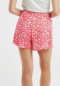 Shorts floraux rouges avec un taille élastique, ornés d'un imprimé de fleurs blanches, en tissu lisse et offrant une coupe décontractée et fluide.