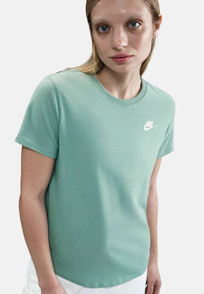 Femme portant un t-shirt Nike vert menthe avec le logo blanc sur la poitrine, se tenant devant un fond clair.