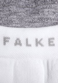 Chaussettes tricotées blanches et grises, avec une bordure côtelée, portant le nom de la marque "FALKE" imprimé en gris sur la plante. Texture douce et design sans couture.